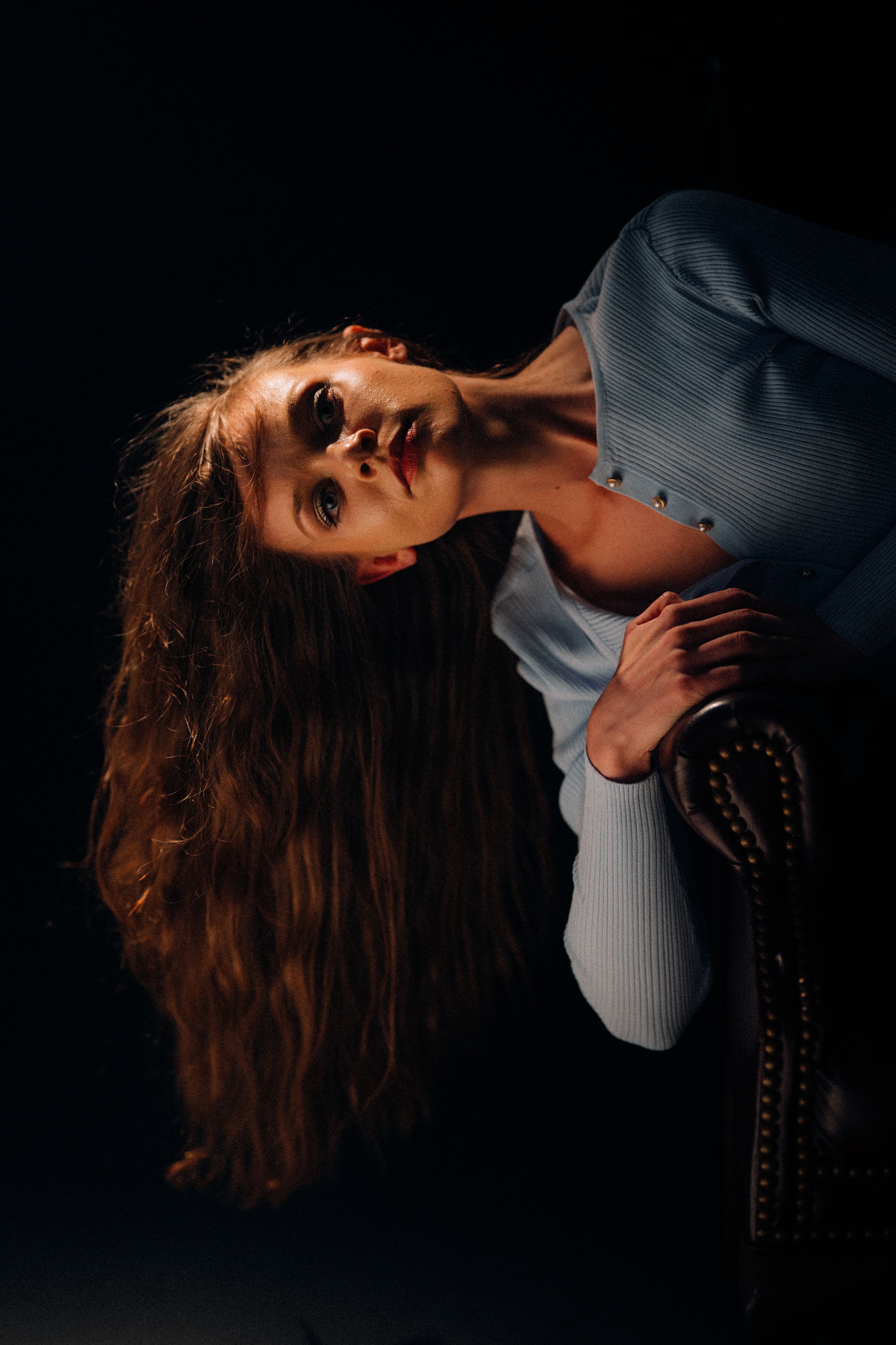 Dramatic portrait series of a person with long hair in a grey top against a black background.