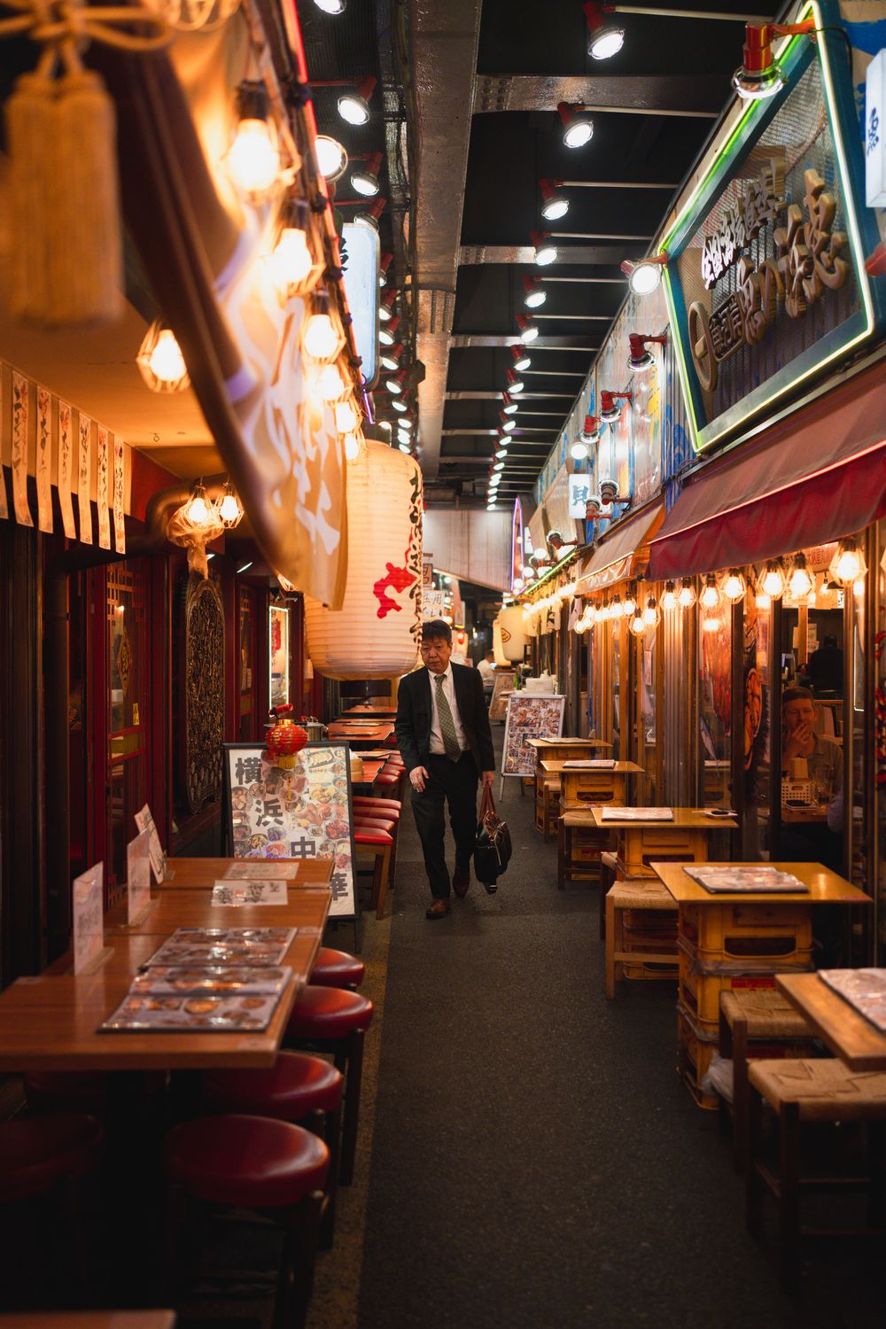 Indoor Japanese dining alley with red lanterns and empty wooden tables.