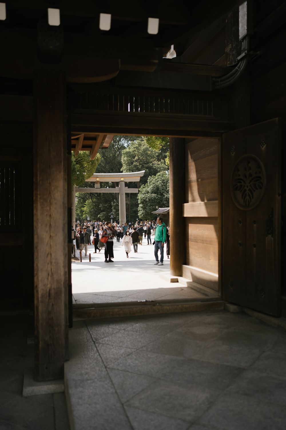 View through a traditional Japanese temple gate showing a torii gate and crowd of visitors in the distance.