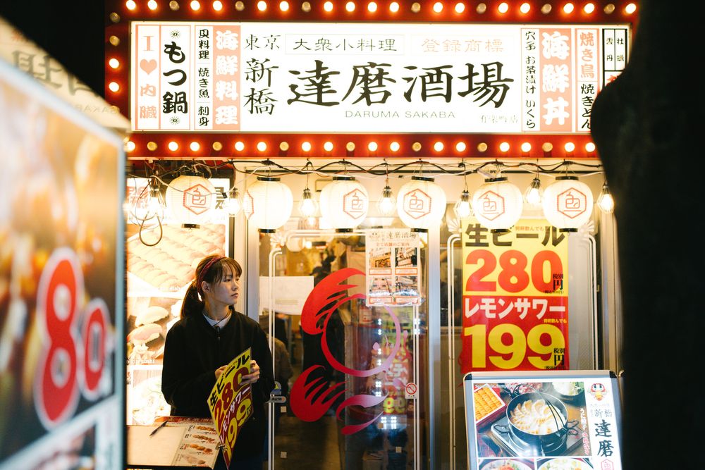 Bright neon signs and storefront of a Japanese sake bar at night.