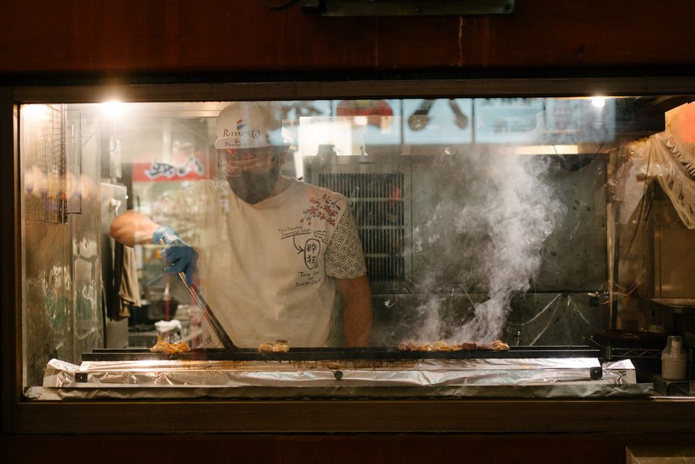 Steam rises from food stalls at an outdoor Japanese market at night.