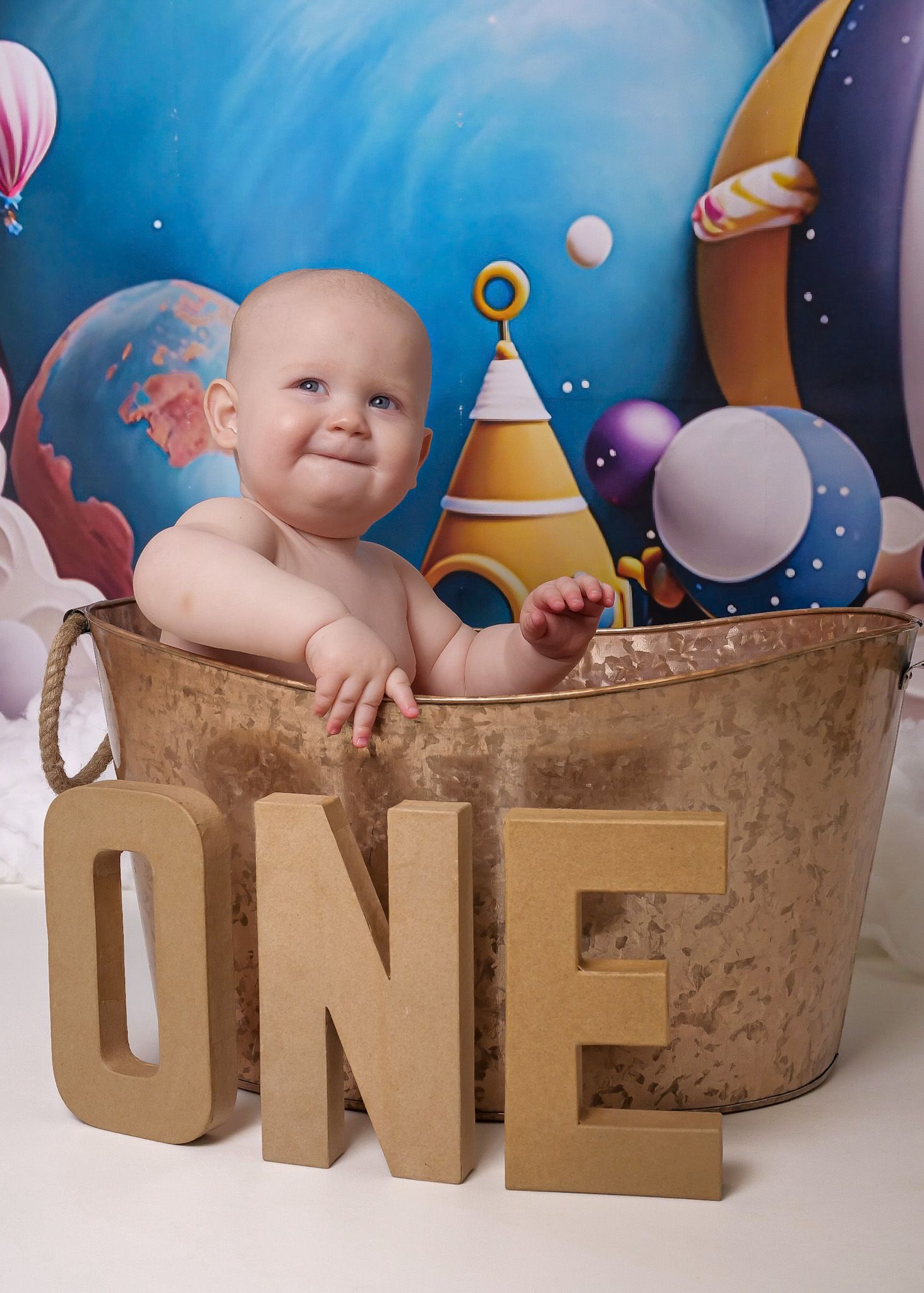 Smiling baby poses in vintage metal tub with cosmic background and gold ONE decoration.