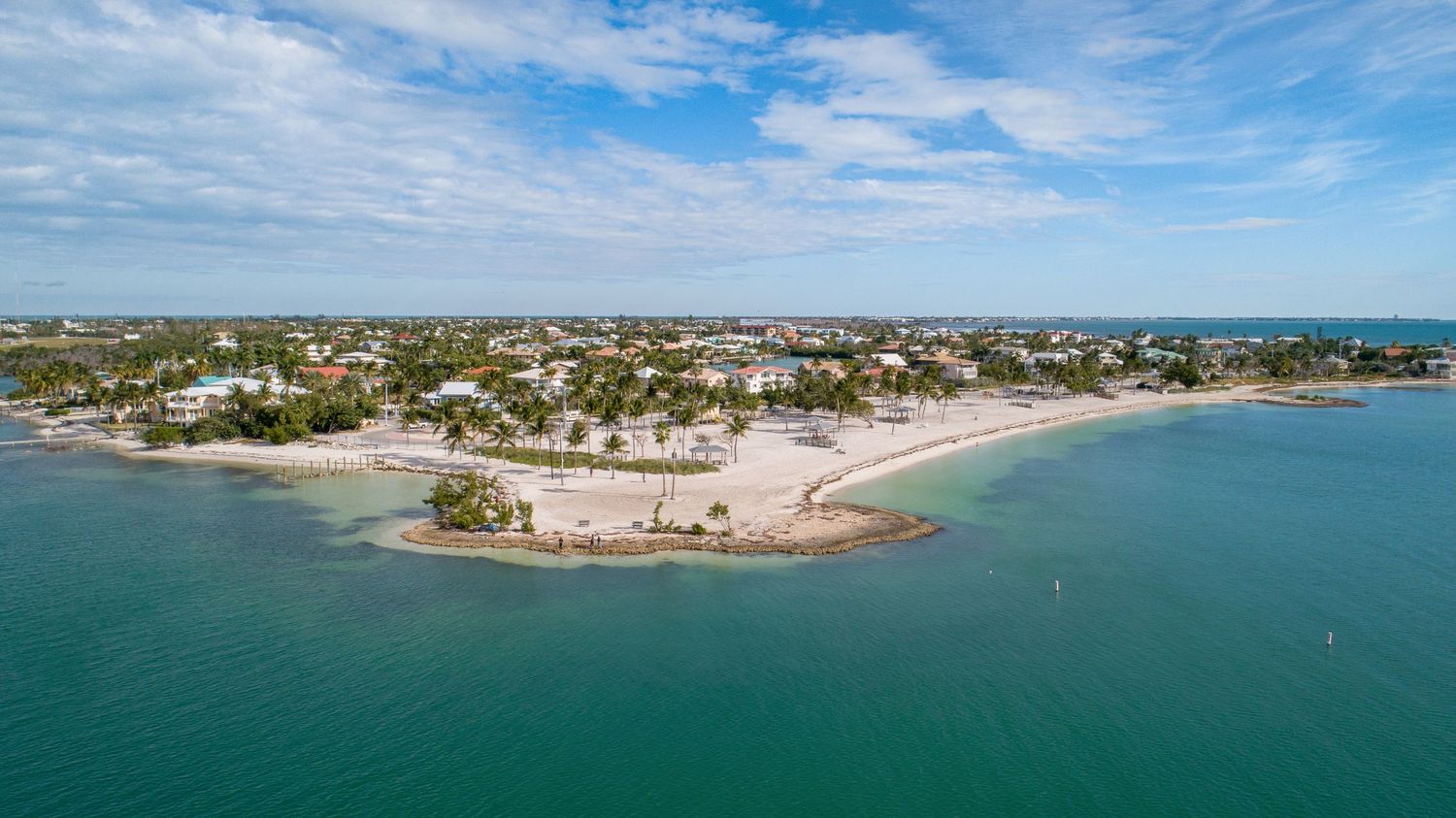 Panoramic aerial view of a coastal town with beaches and waterfront properties under blue skies.