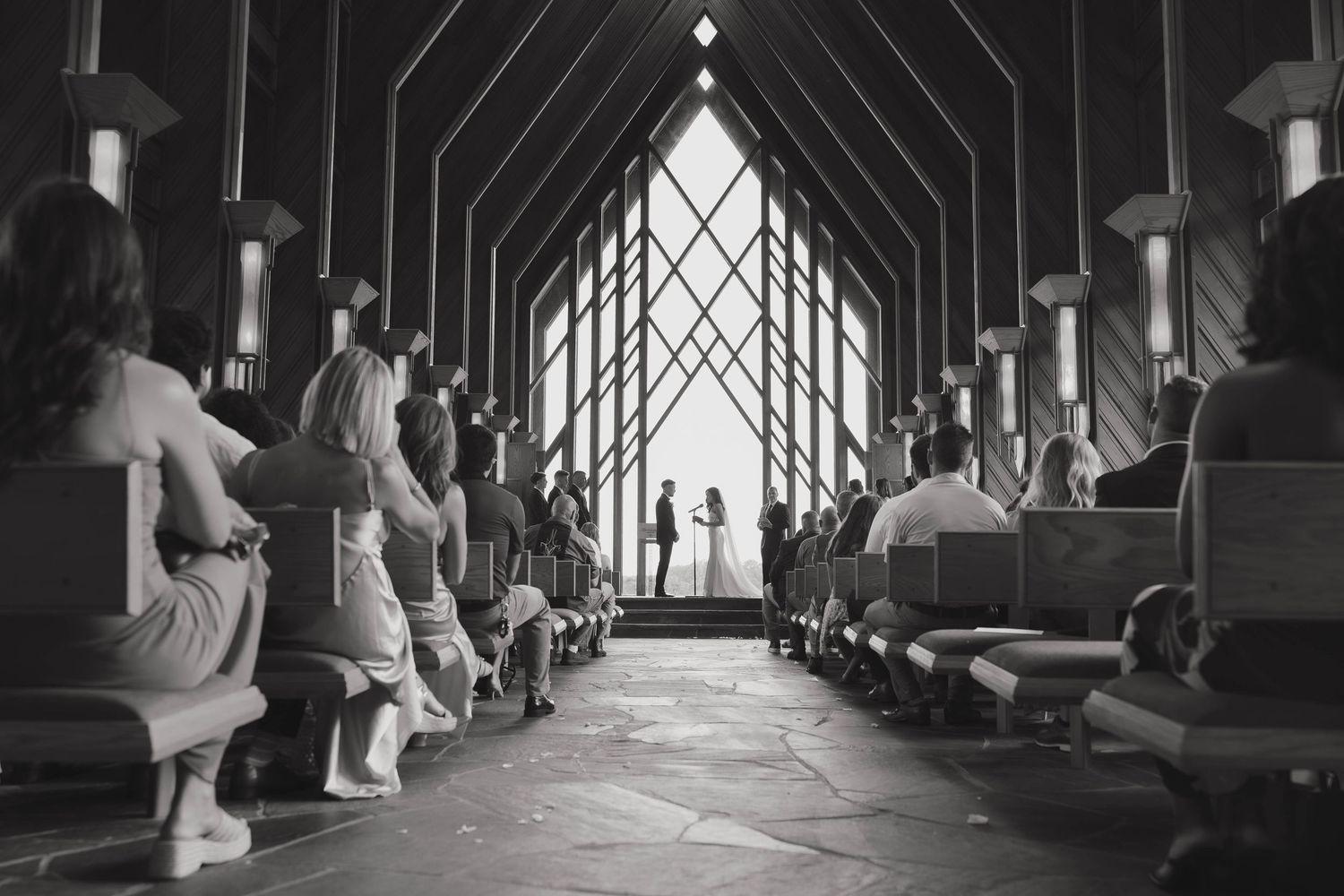 People walk through a covered bridge corridor with sunlight streaming in through arched openings.