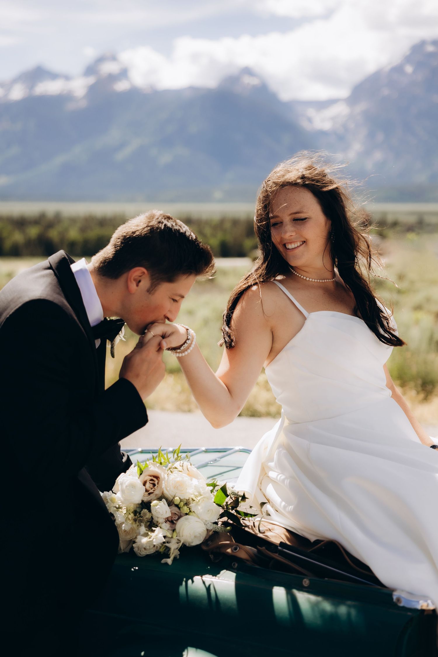 A romantic wedding photo series shows a couple embracing against a backdrop of majestic mountains and open plains.