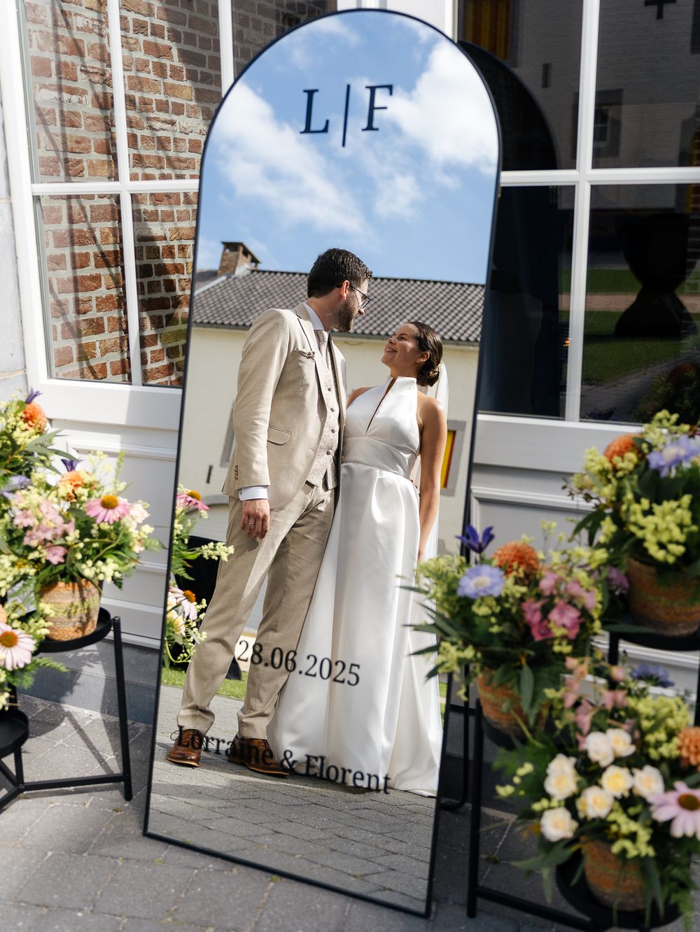 Photos de mariage prises près de l'entrée d'un bâtiment en briques décoré de fleurs et d'un miroir. Florent Vause
