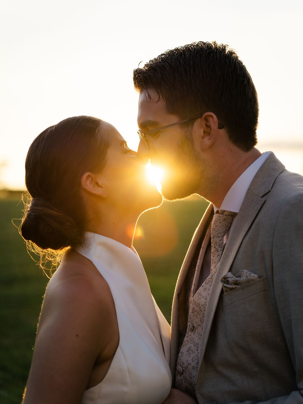 Silhouettes romantiques se découpant sur un coucher de soleil éclatant, vêtues de tenues de mariage formelles. Florent Vause