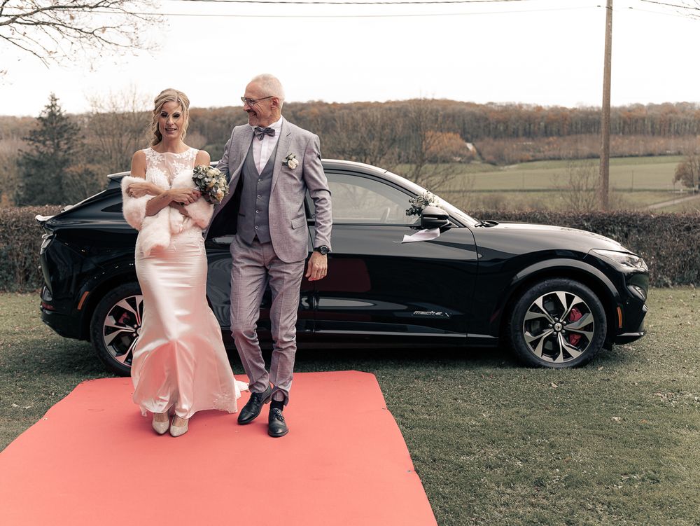 Couple de mariés posant sur un tapis rouge à côté de voitures de luxe dans un décor champêtre. Florent Vause