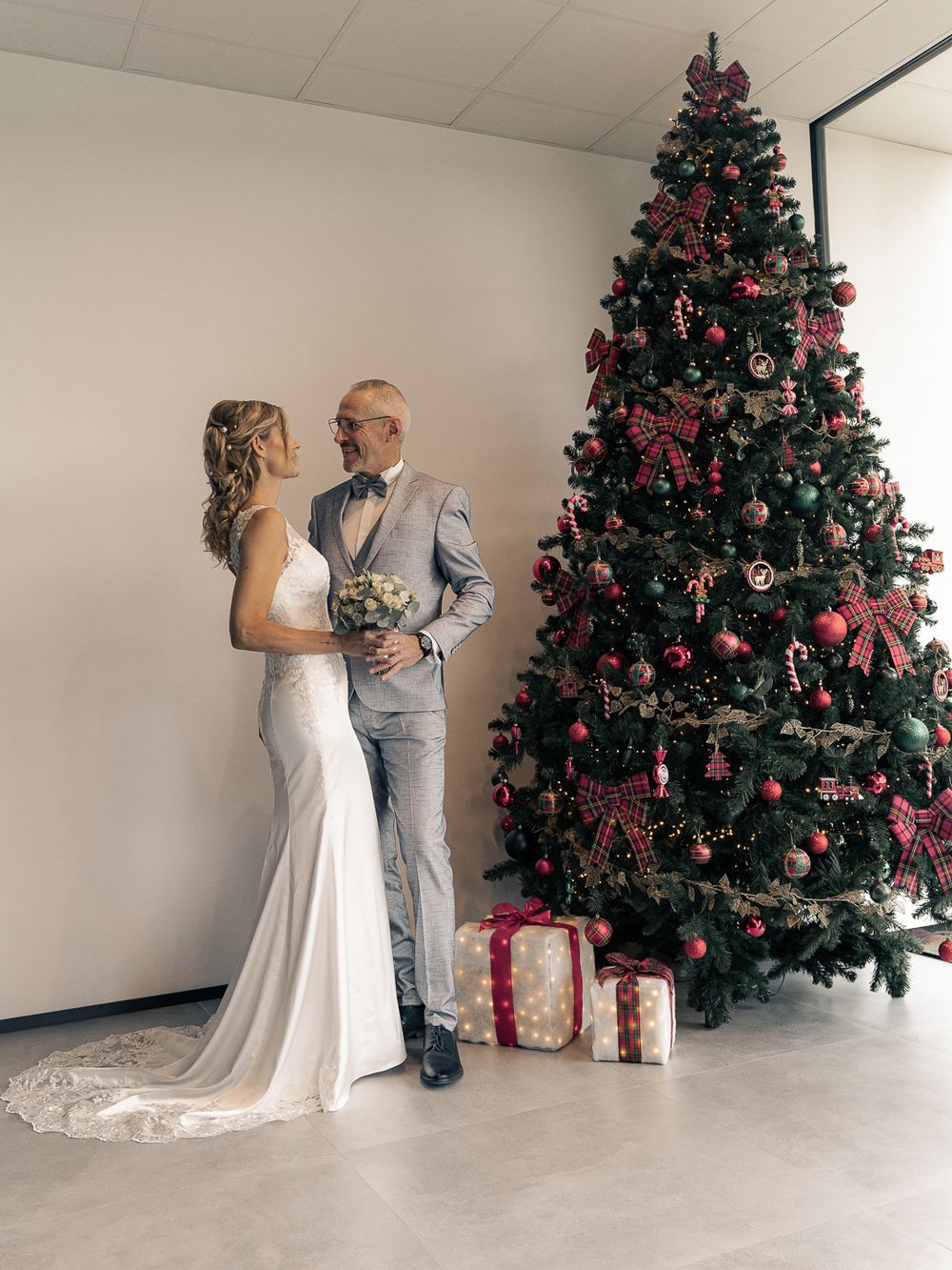 Une séance photo de mariage près d'un sapin de Noël décoré, avec des cadeaux emballés à ses pieds. Florent Vause