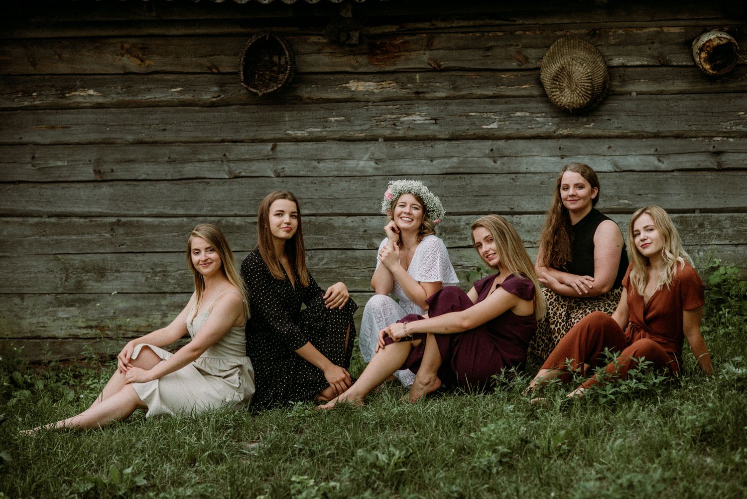 Friends relaxing together against a rustic wooden wall in casual summer outfits.