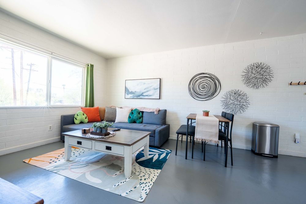 Modern living room with gray sofa, colorful pillows, geometric rug and white walls decorated with circular wall art.