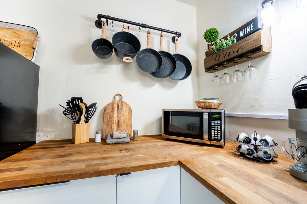 Modern kitchen corner with butcher block countertops, white cabinets, hanging pots and floating shelves.