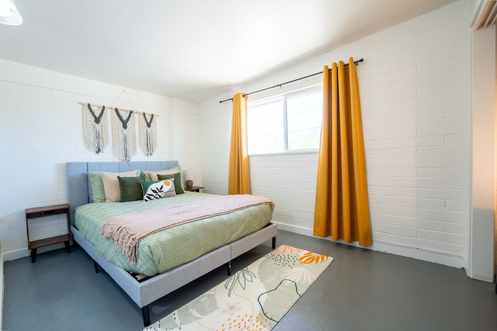 Bright bedroom featuring mustard yellow curtains, gray bedding, and decorative wall art above the bed.