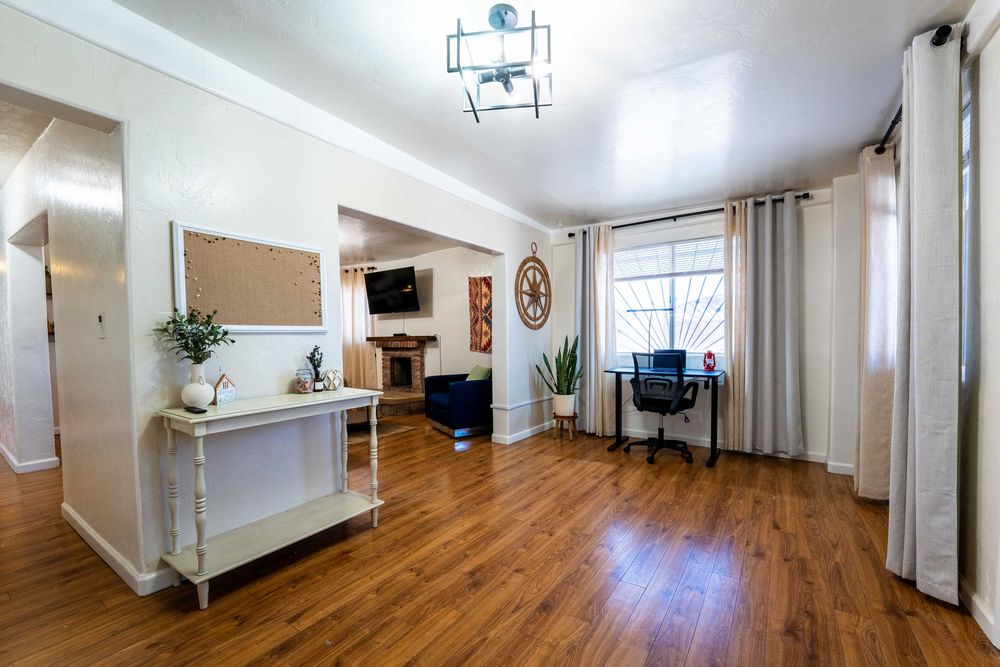 Modern living room with hardwood floors, white console table, flat screen TV, and floor-to-ceiling curtains.