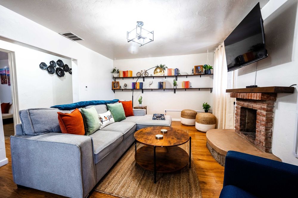 Modern living room interior with gray sectional sofa, hardwood floors, decorative shelving, and bright natural lighting.
