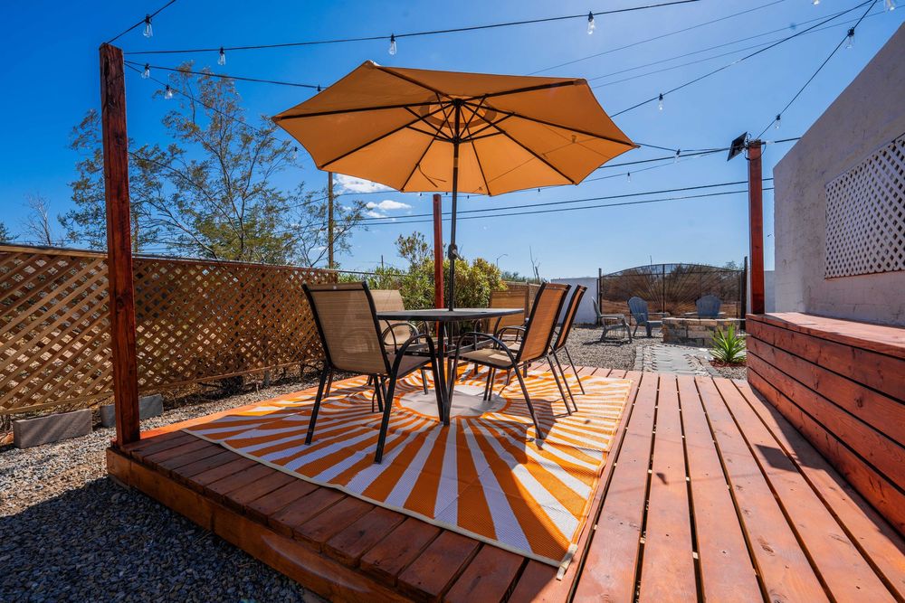Wood deck patio with orange umbrella and dining set overlooking desert landscape on sunny day.