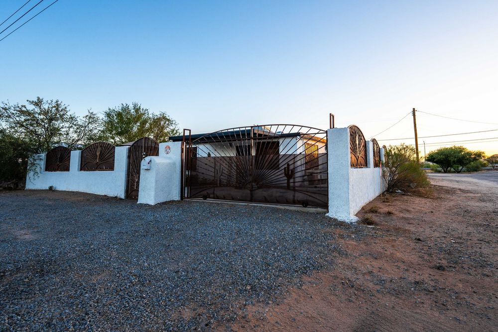 White stucco house with brown gate entrance on gravel driveway at dusk in desert setting.
