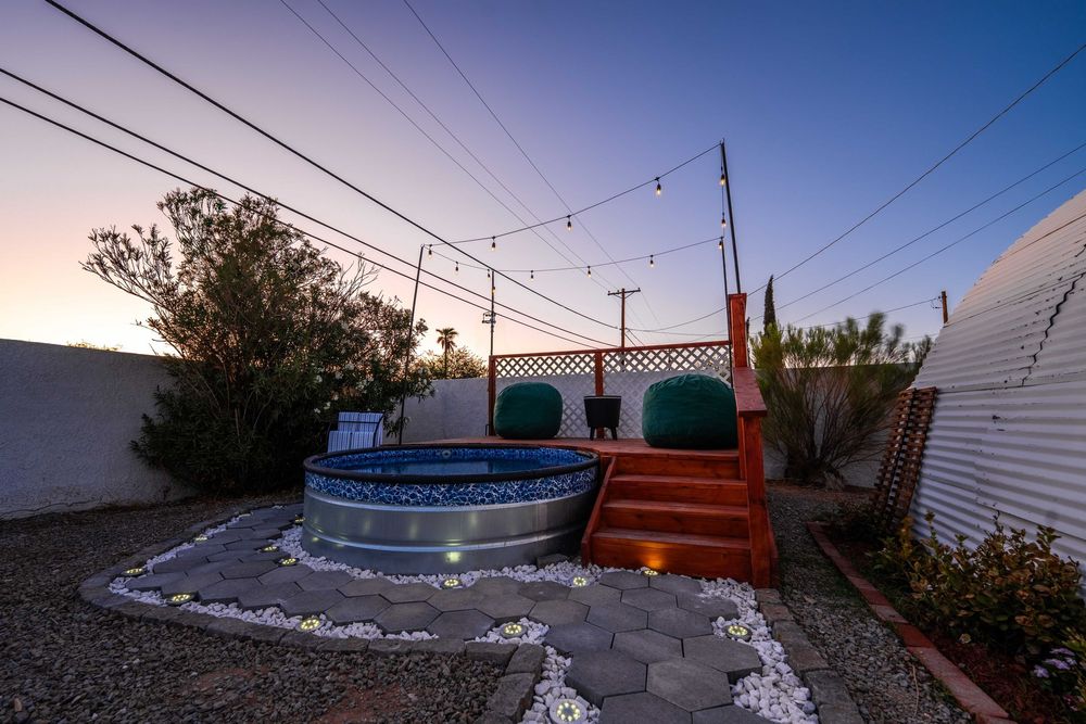 Backyard seating area with colorful chairs and hot tub under power lines at sunset.