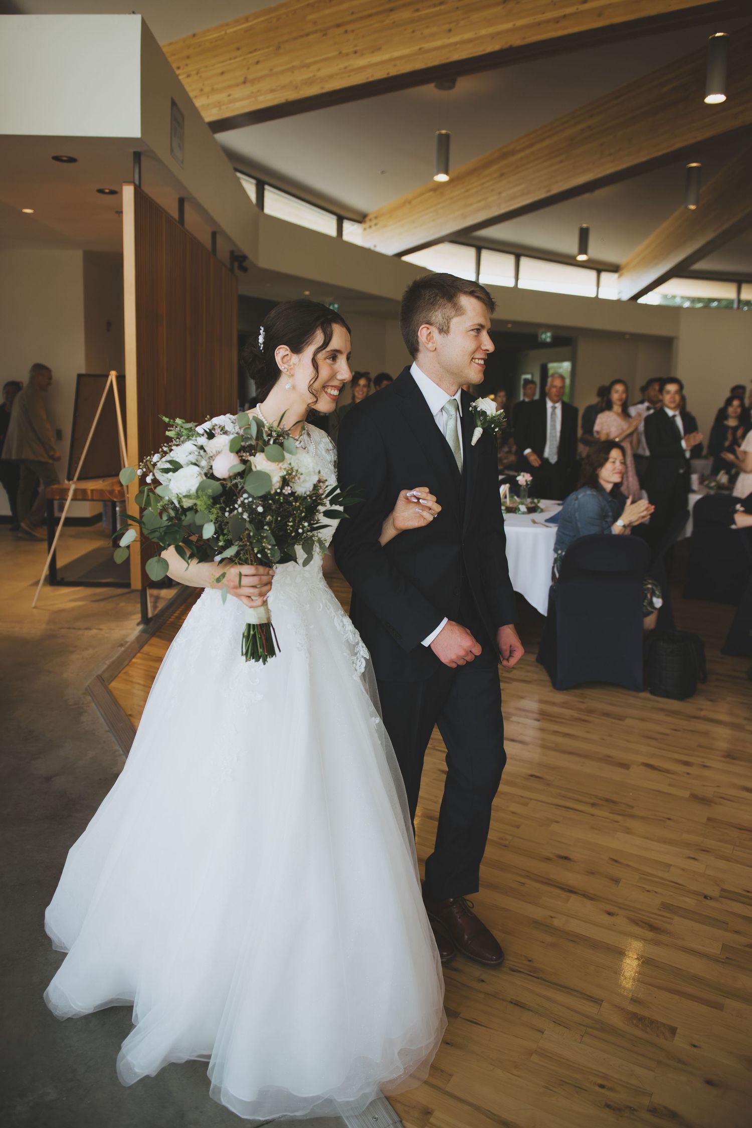 A couple walks arm in arm at their wedding ceremony in a wood-paneled venue with vaulted ceilings.