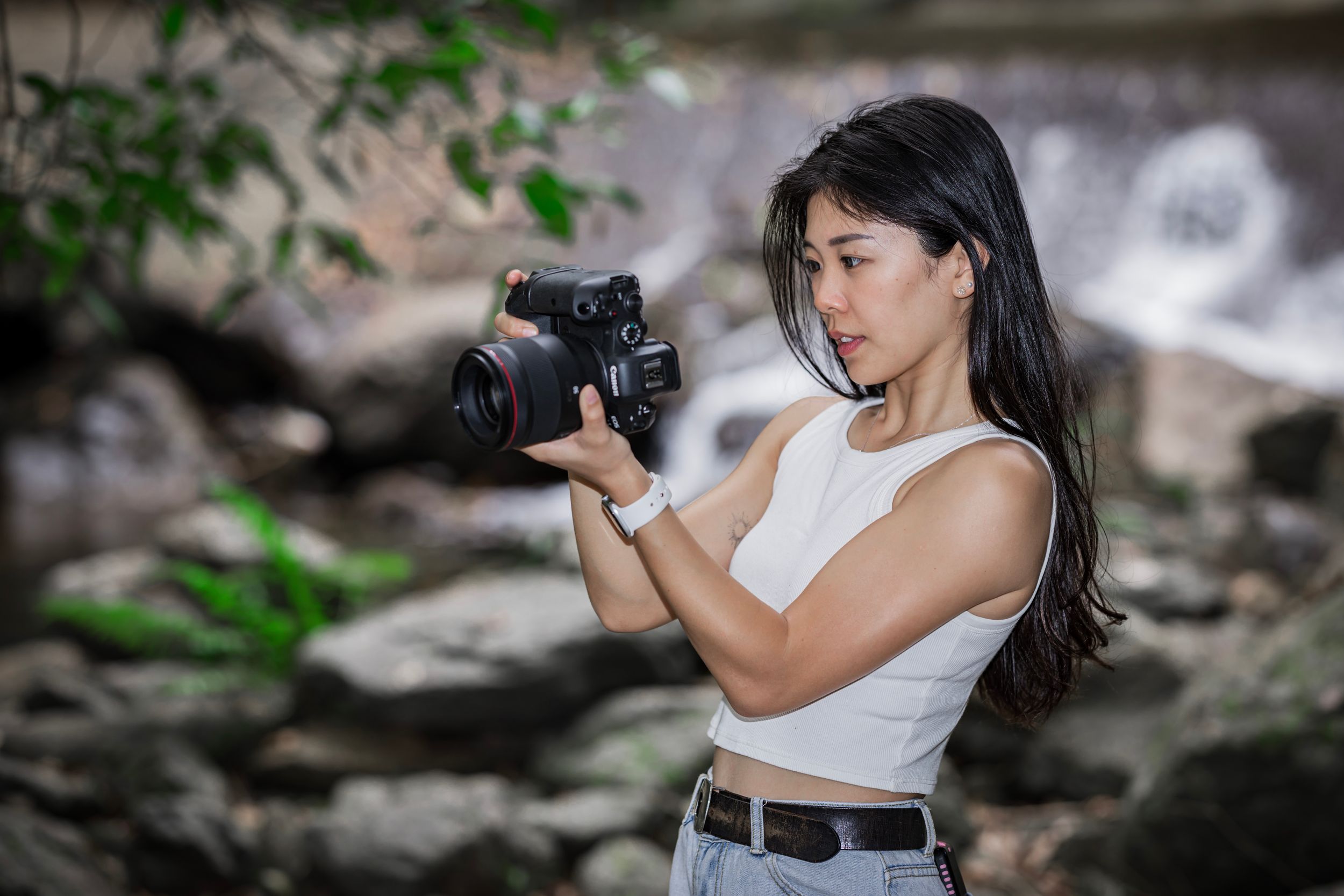 Professional photographer wearing white dress taking photos in outdoor natural setting with professional camera equipment.