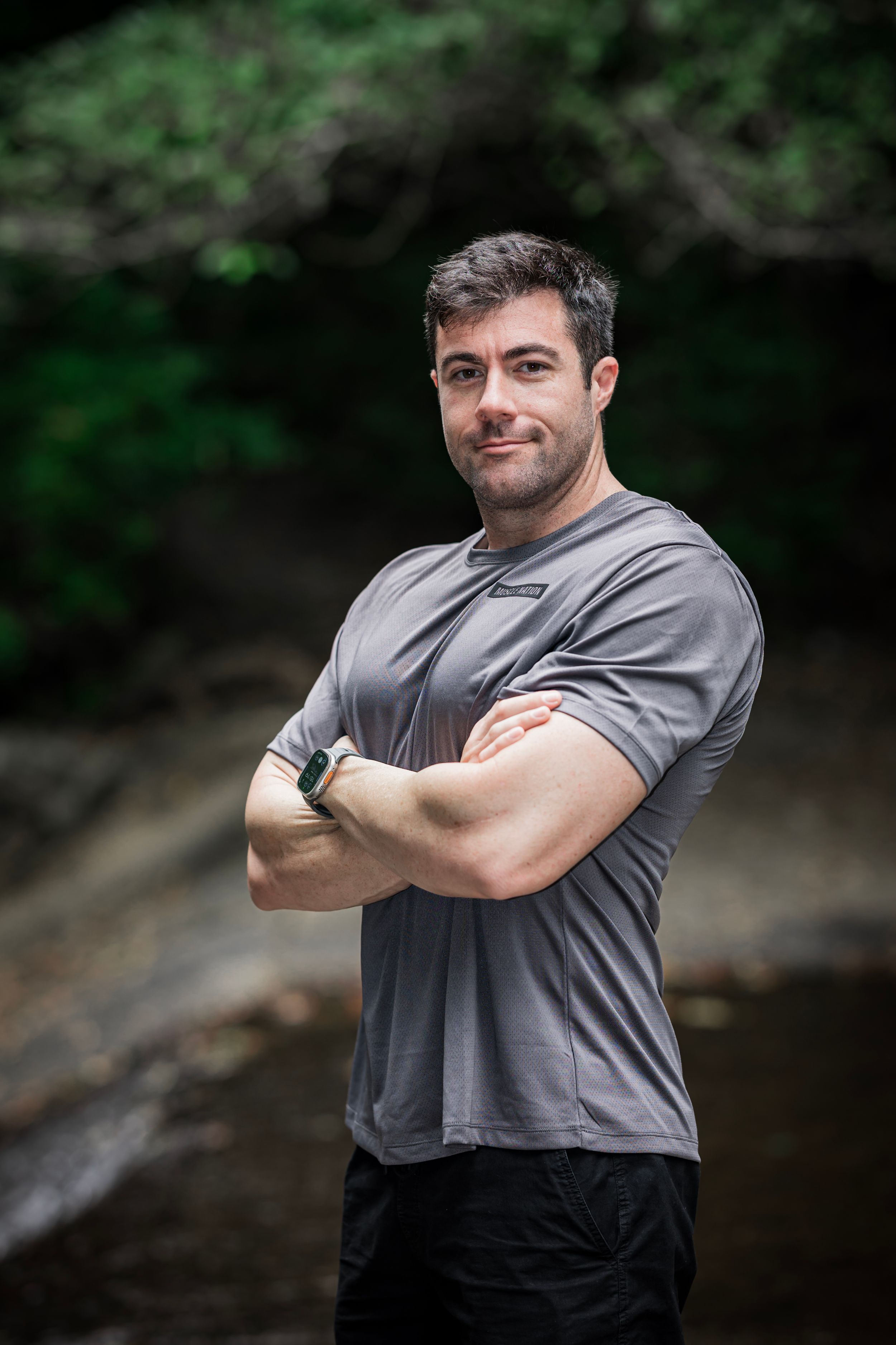 Person in gray t-shirt demonstrating different poses against a natural outdoor backdrop with rocks and foliage.
