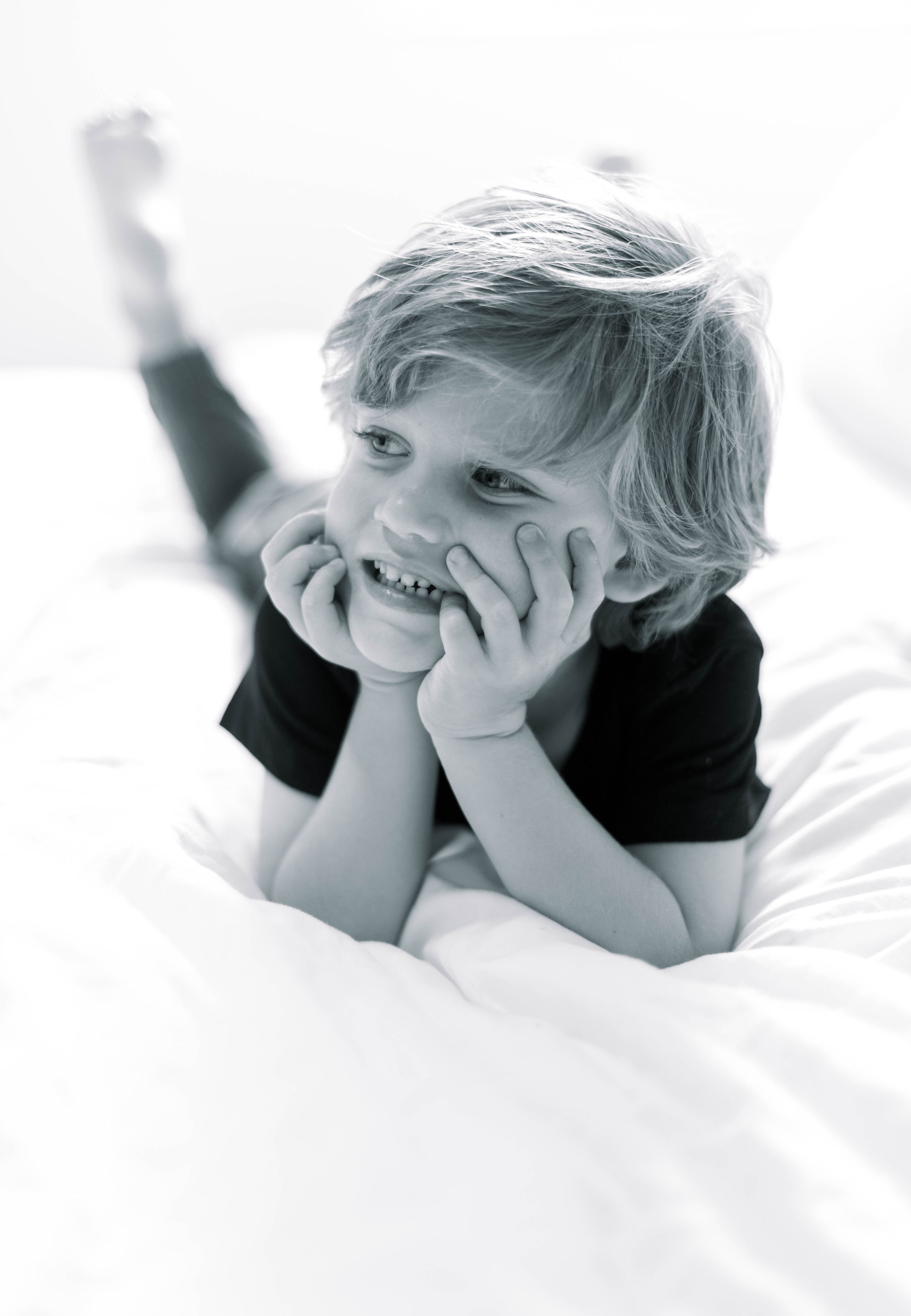 Series of three black and white photos showing a child lying on white bedding while playing peek-a-boo.