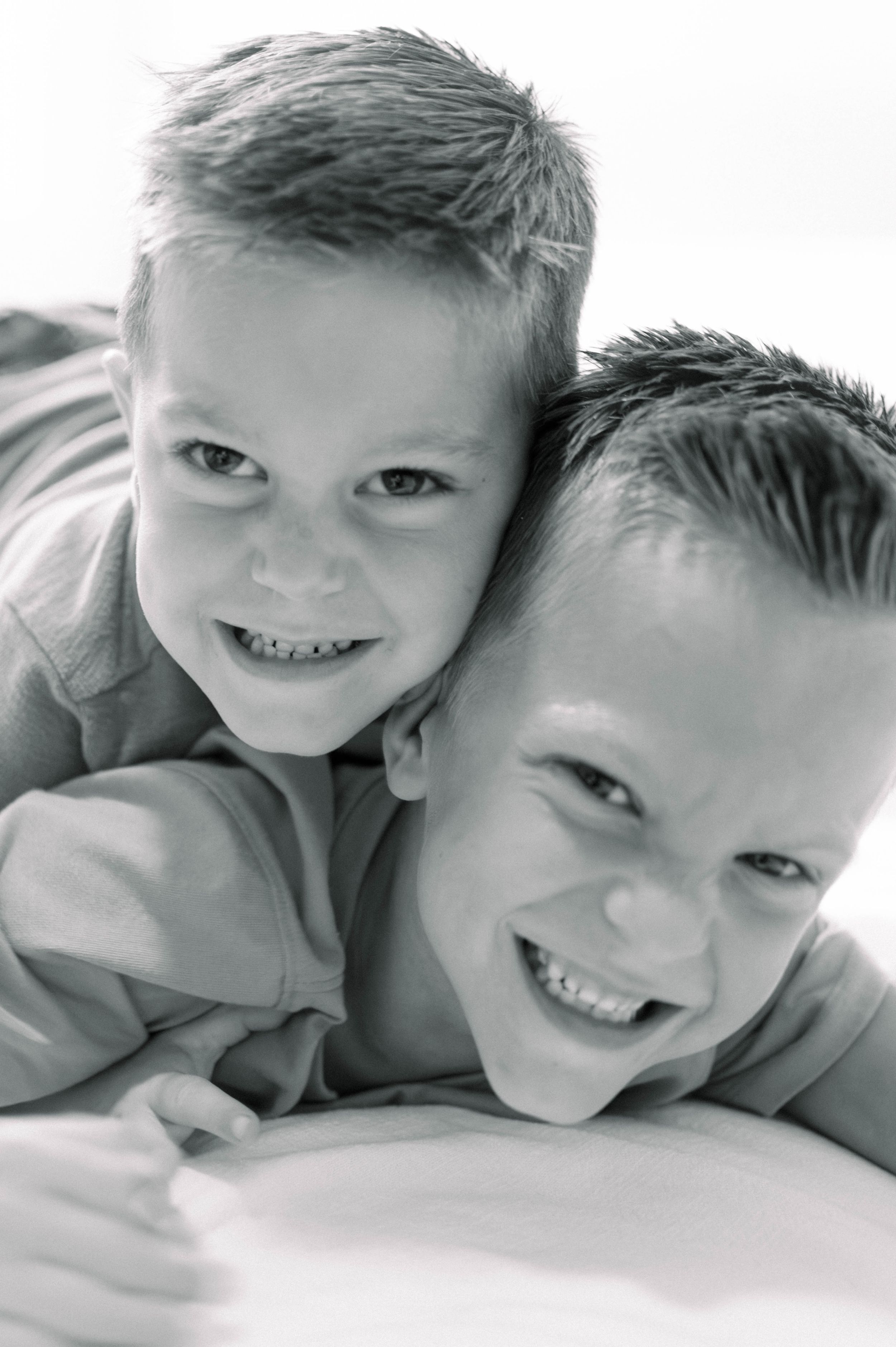 Black and white portraits showing affectionate siblings lying together with happy expressions showing close bond.
