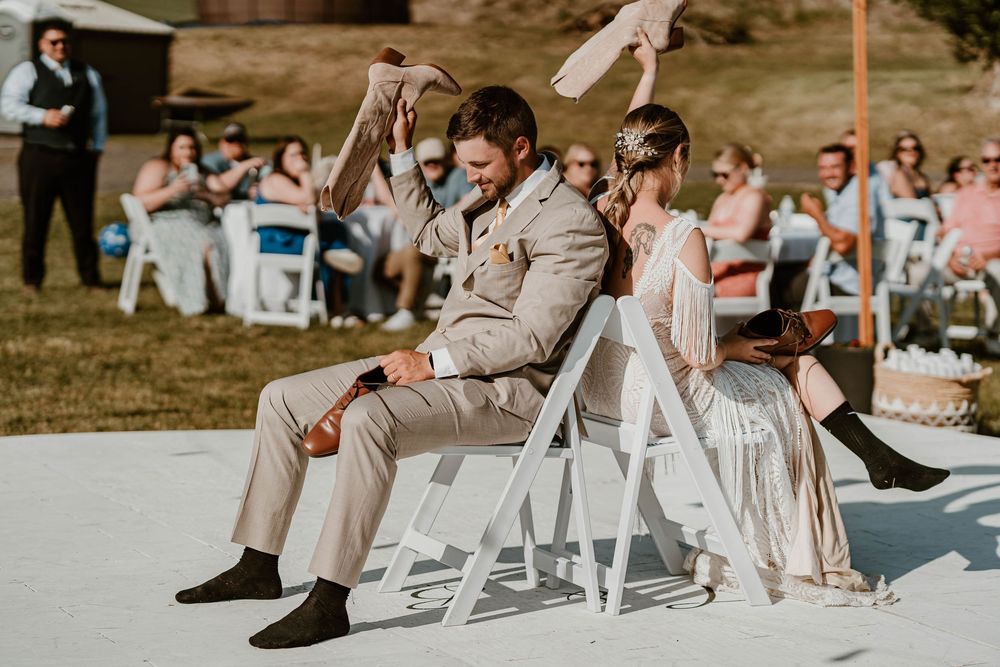 Bride and groom playing the shoe game at outdoor wedding reception seated back to back.