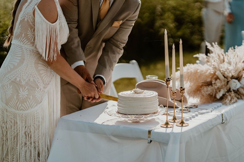 Bride and groom cutting white wedding cake at outdoor reception table with gold candlesticks.