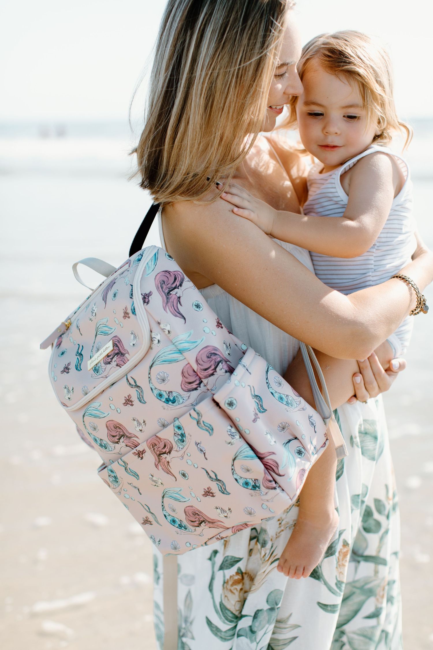 Mother holding child on beach in matching butterfly print outfits.