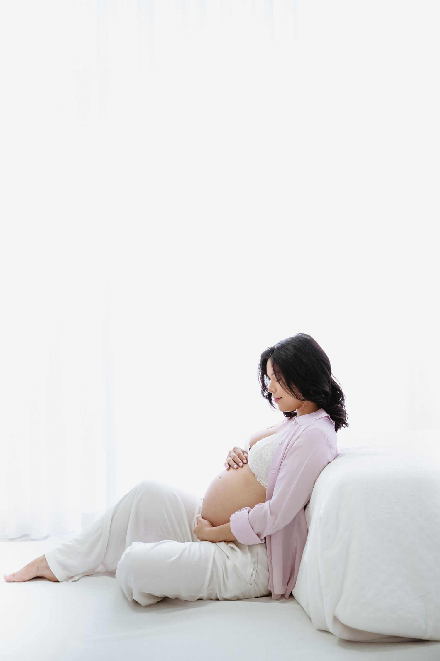 Four sequential maternity photos showing a woman in soft pink and white clothing reclining on a white backdrop.