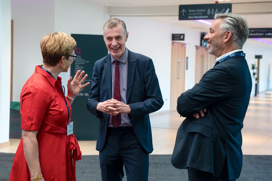 Three professionals in formal attire engaged in conversation at a modern conference venue.
