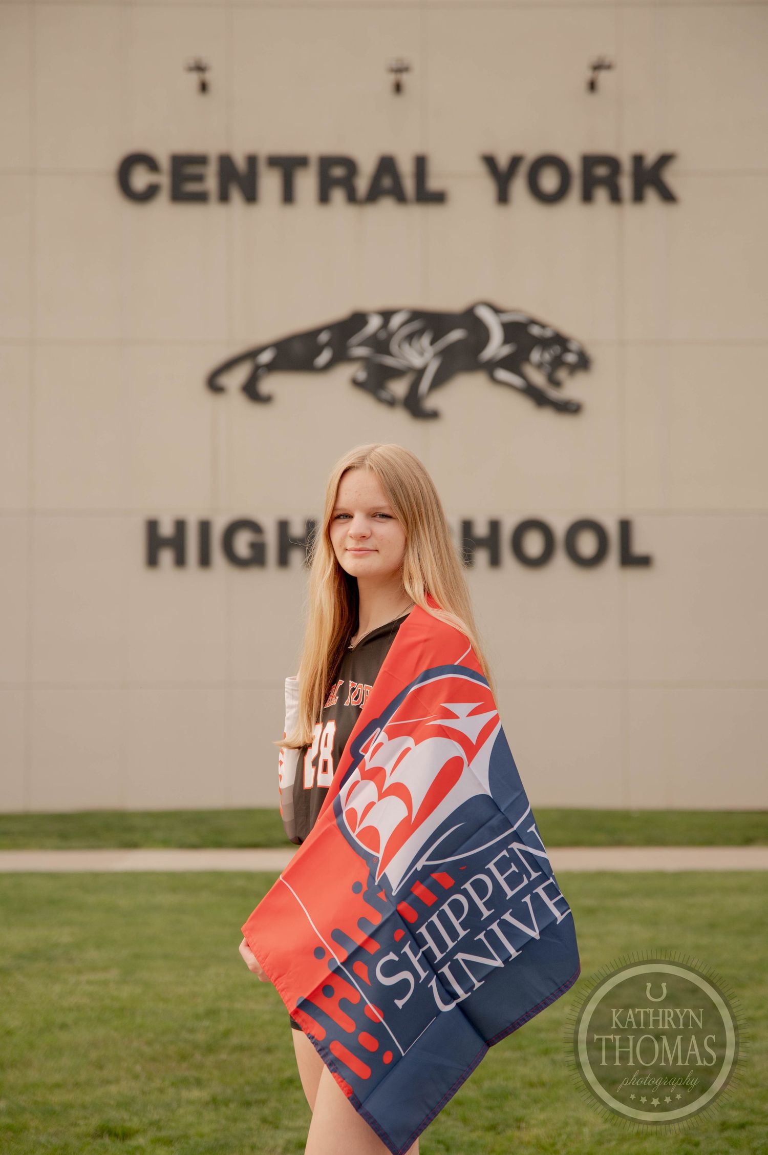 Student stands outside Central York High School holding a navy and red school banner on the lawn.