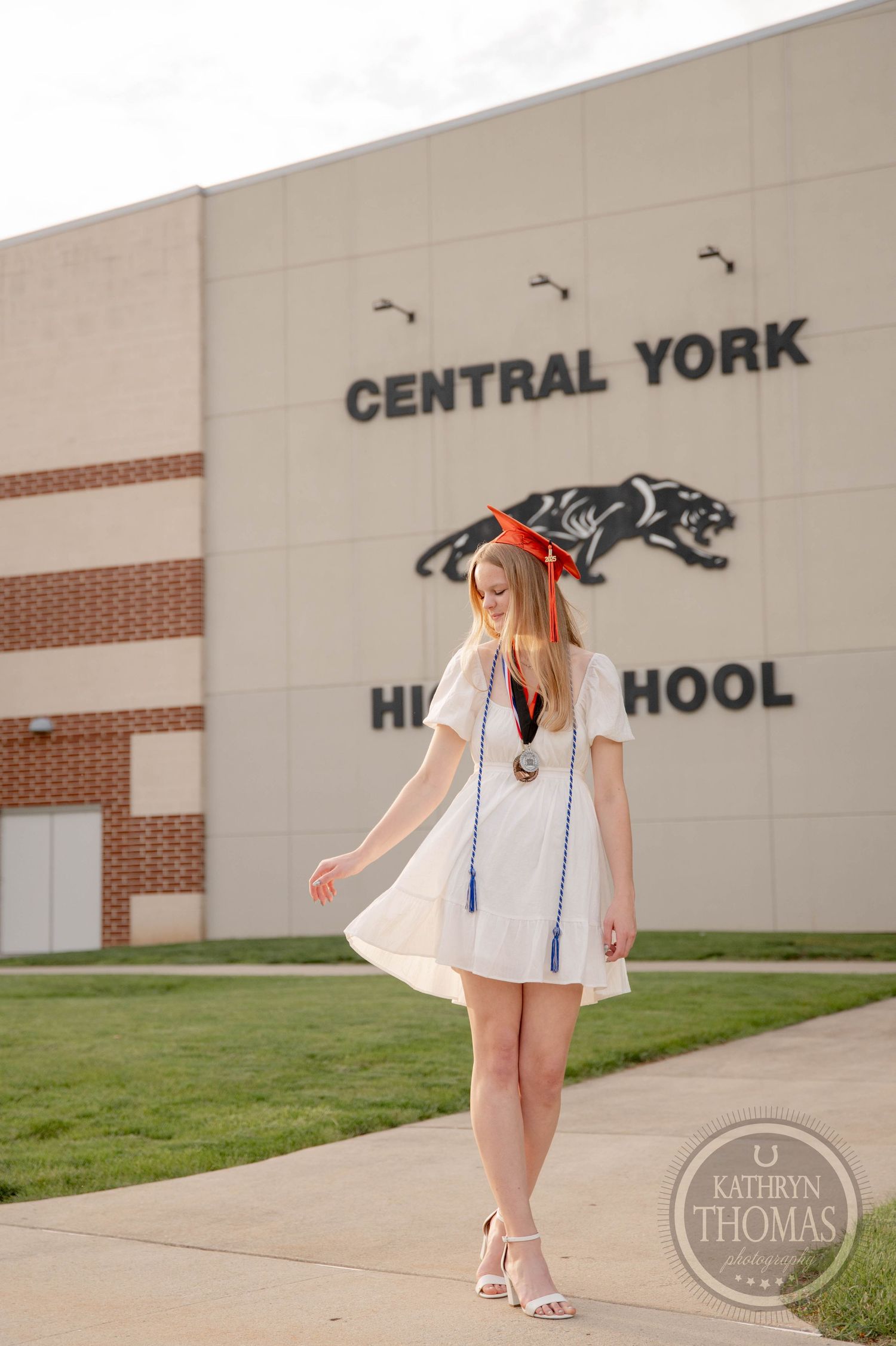 A student in a white dress stands in front of Central York High School during graduation photos.
