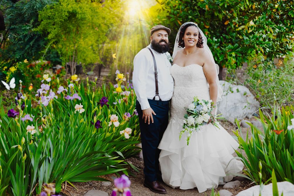A couple poses in a lush garden with blooming yellow irises and spring flowers during an outdoor wedding photoshoot.