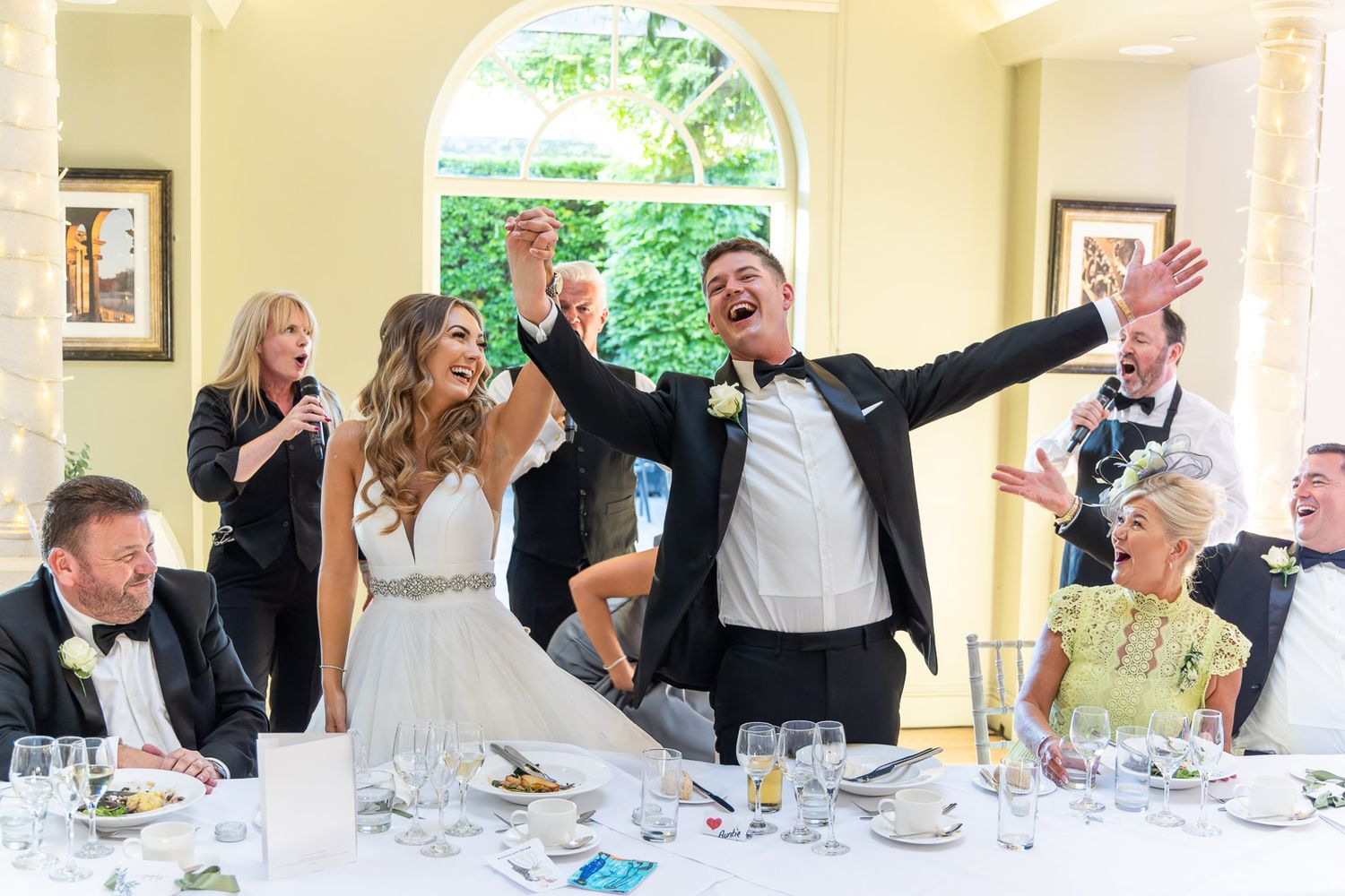 Celebratory moment at an elegant Kent wedding reception with guests cheering and raising their hands in joy at a formal banquet table.