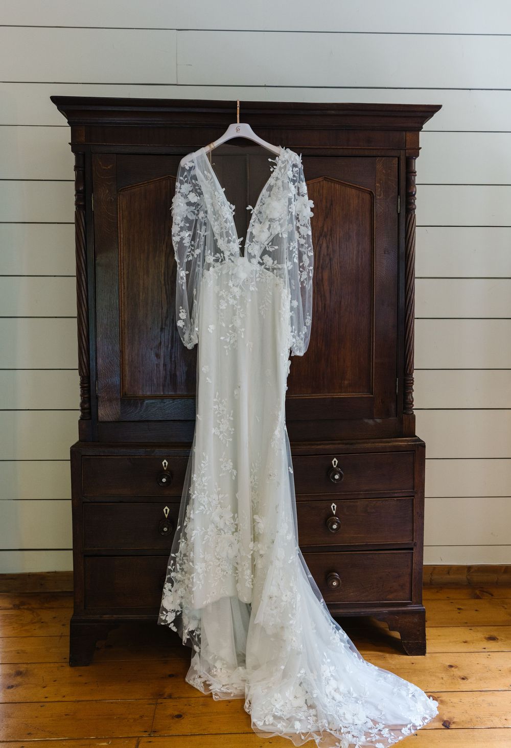A sequence showing a vintage white lace wedding dress displayed against a dark wooden wardrobe on hardwood floors.