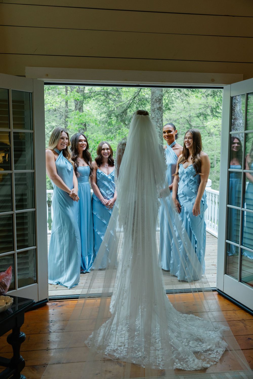 A wedding dress reveal moment with bridesmaids in light blue dresses reacting with joy on a sunlit porch. Old Edwards Inn