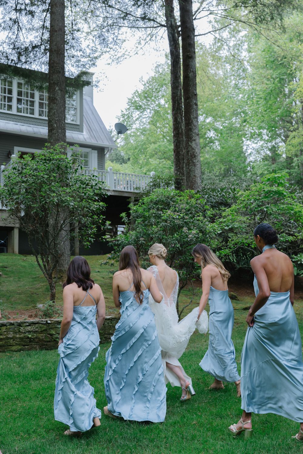 bridesmaids light blue dresses playfully running across a green lawn in front of a house. Old Edwards Inn