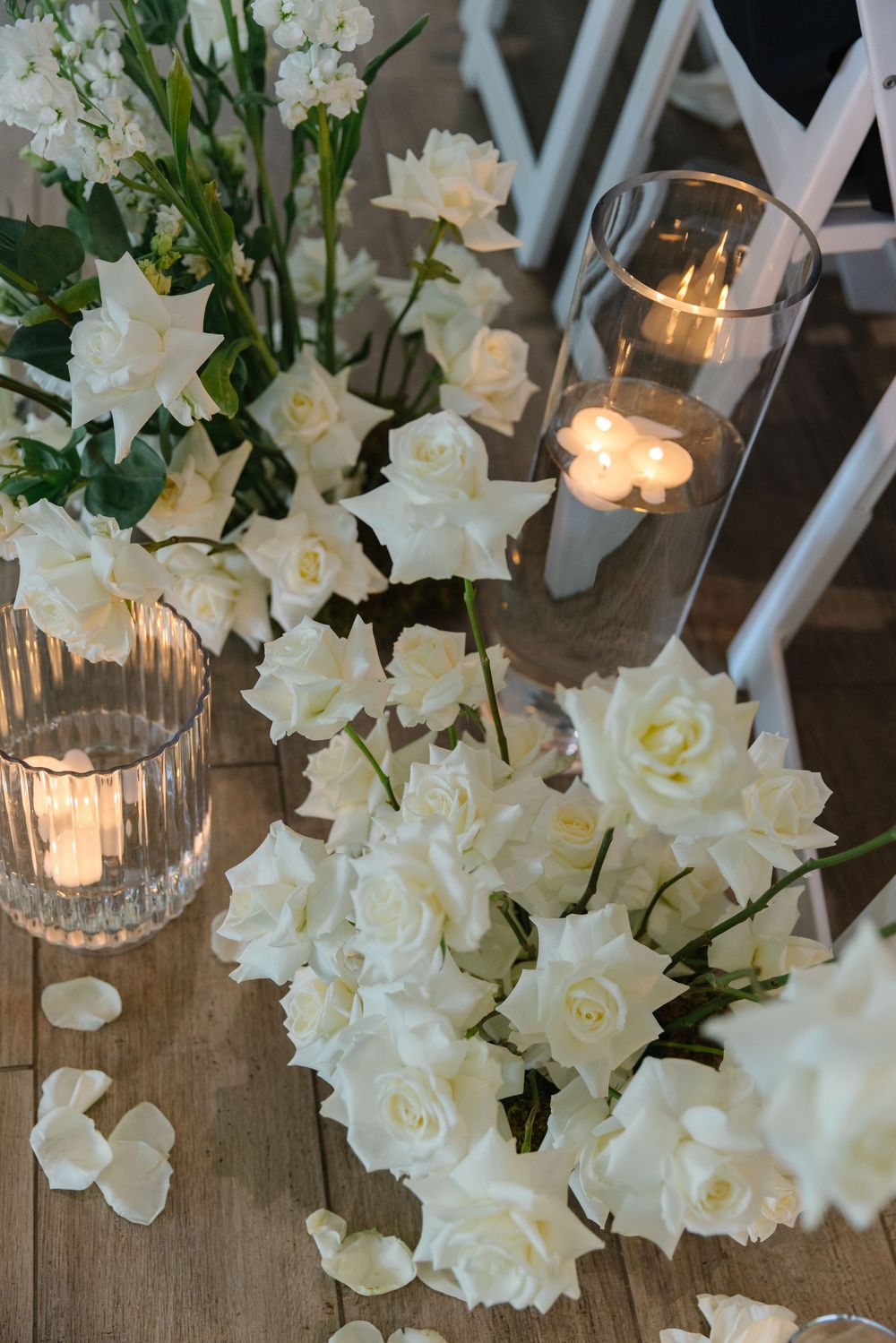 White roses and candles create an elegant table decoration with glowing candlelight reflecting in glass holders.