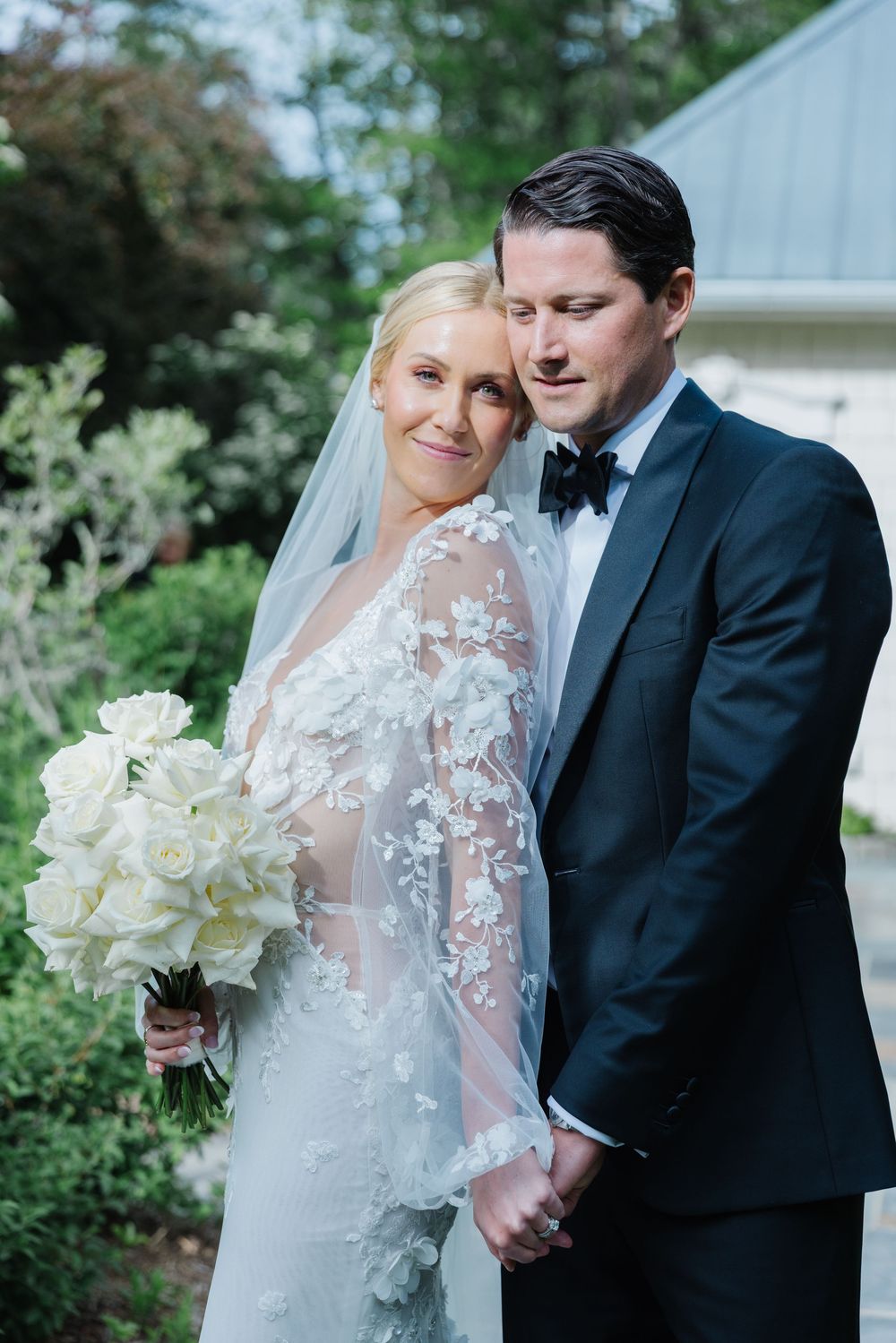 Newlywed couple shares intimate moments in garden setting wearing traditional wedding attire with white floral bouquet. old edwards inn