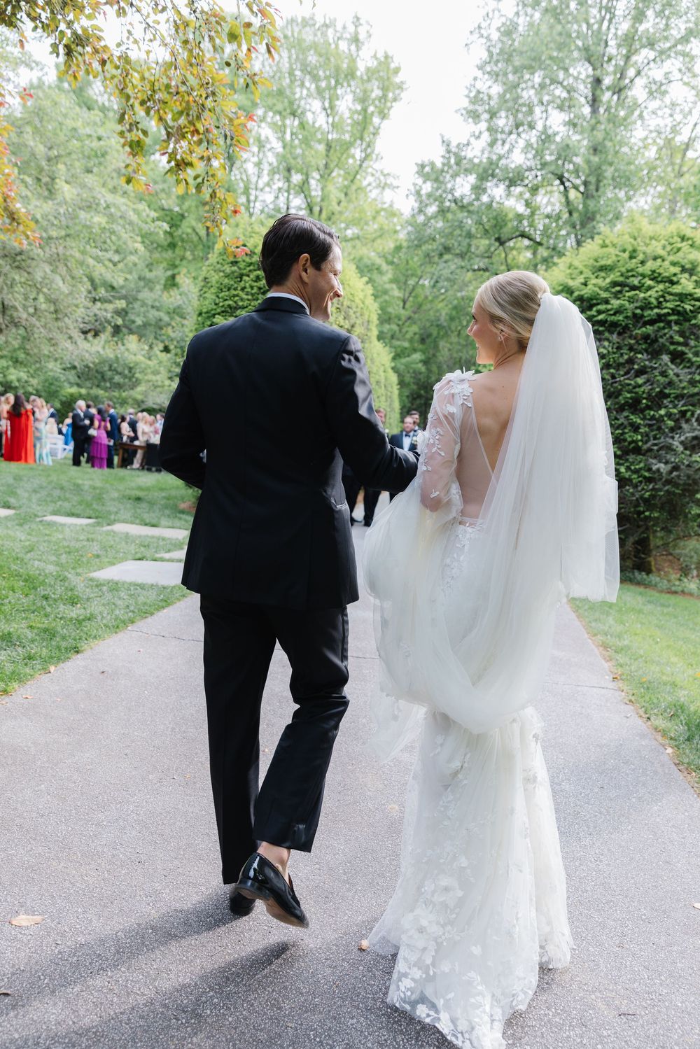 A bride and groom walk down a garden path surrounded by autumn trees during their outdoor wedding ceremony. old edwards inn