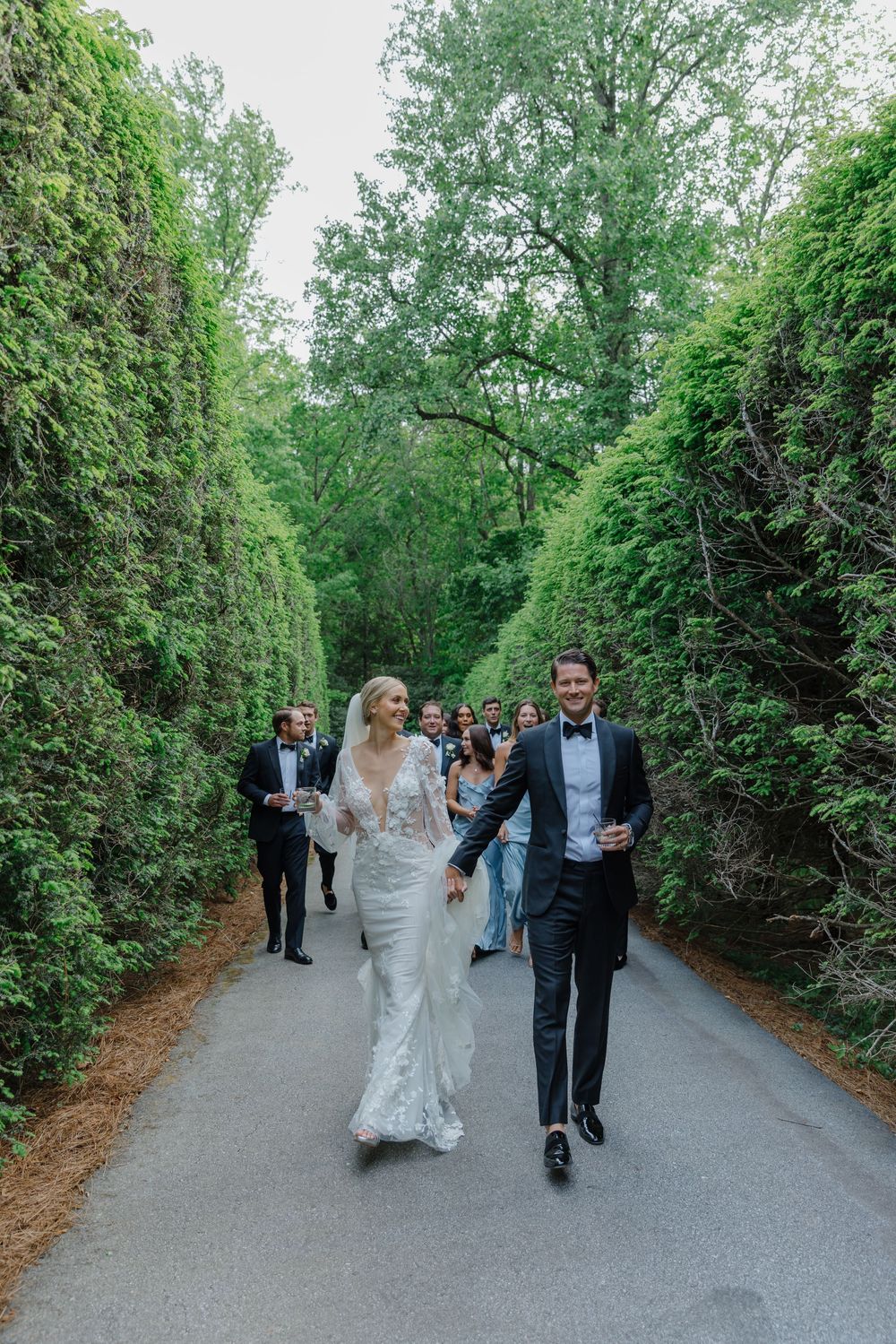 Wedding party walks along a tree-lined path at an outdoor venue during a celebration. old edwards inn north carolina
