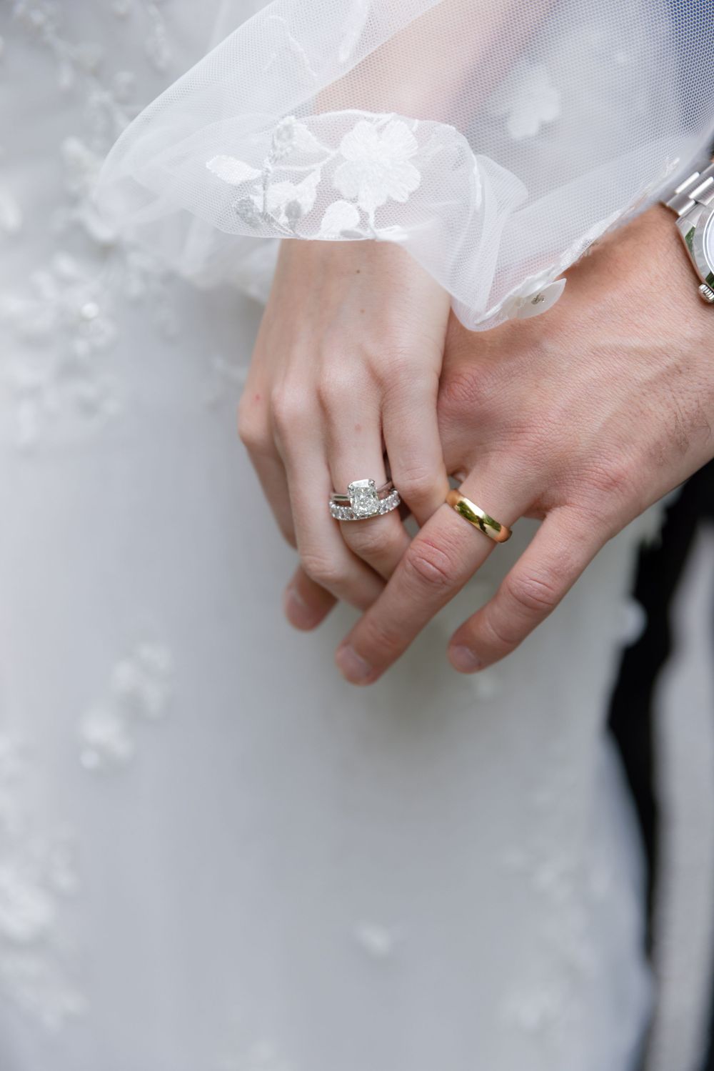 Close-up view of hands wearing elegant wedding rings with white lace fabric in the background. old edwards inn