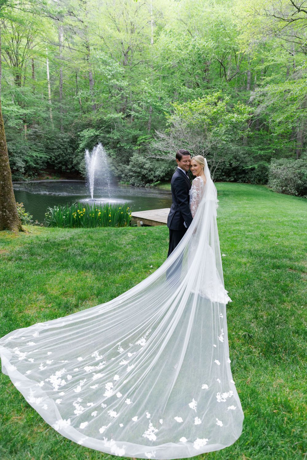 A long white wedding veil with butterfly appliques trails across a green lawn in a romantic outdoor setting.  old edwards inn