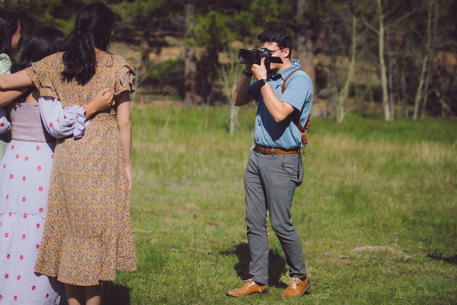 A photographer takes pictures in a grassy field while others hold up flowing fabrics in the background.