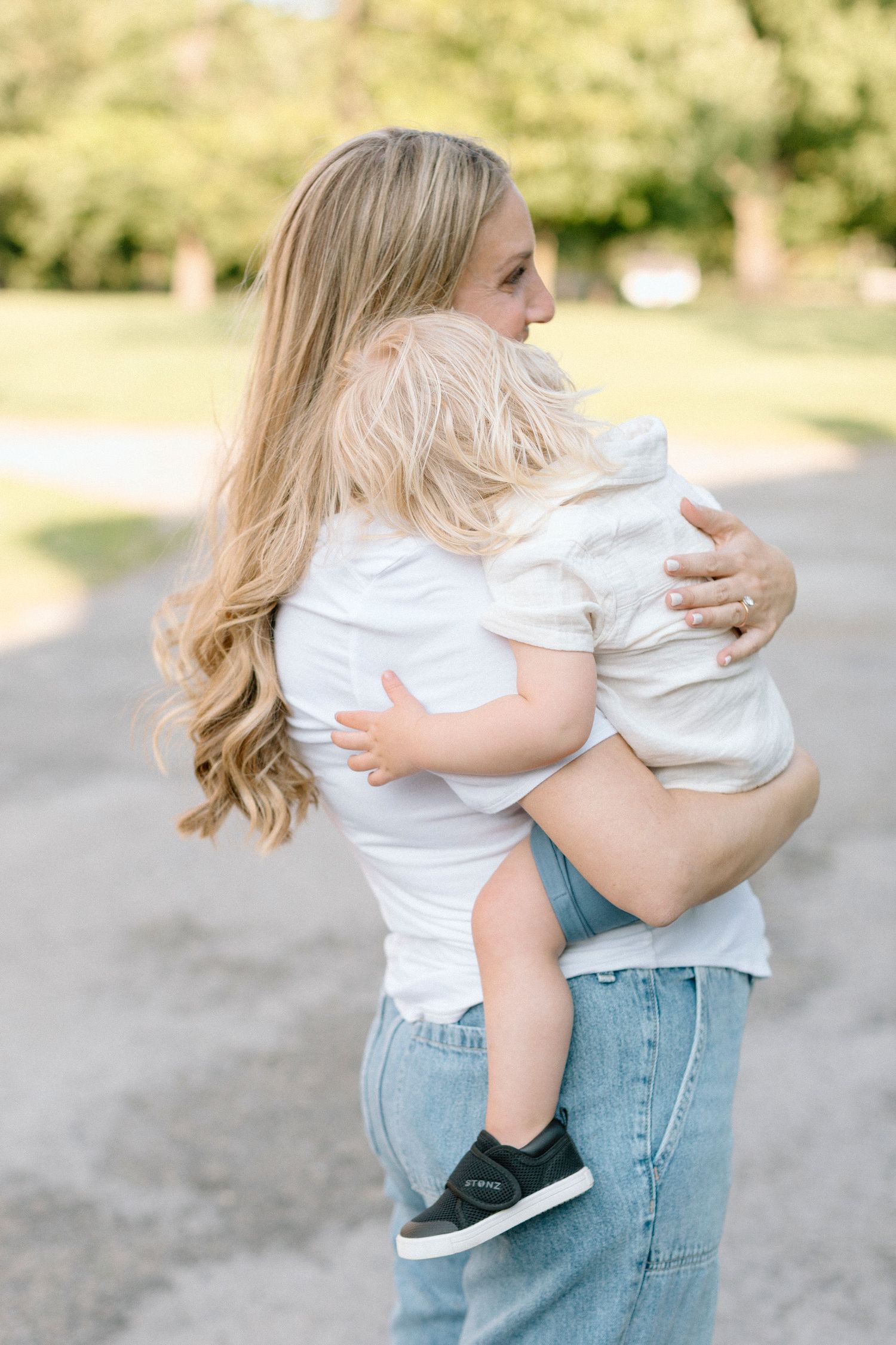 Tender family moment captured outdoors showing embrace in white shirts and denim on a sunny path.