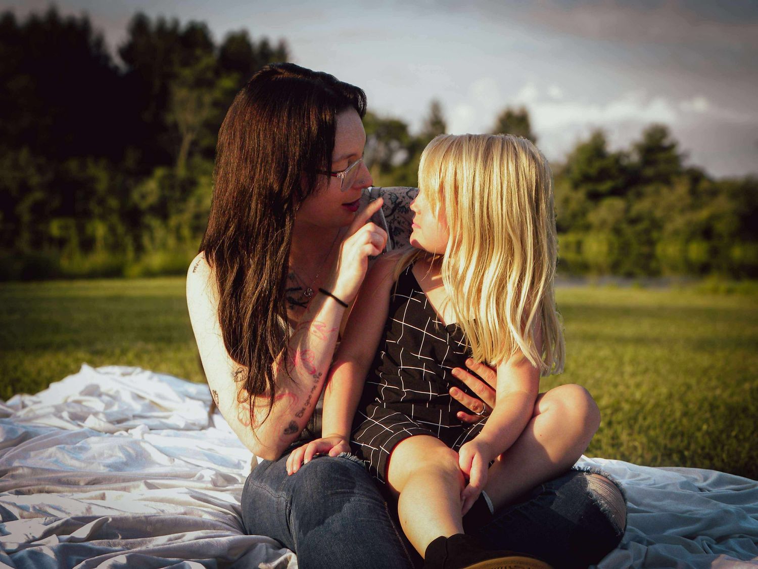 A romantic outdoor photo shoot captured at golden hour showing two people lying on a blanket in a grassy field.