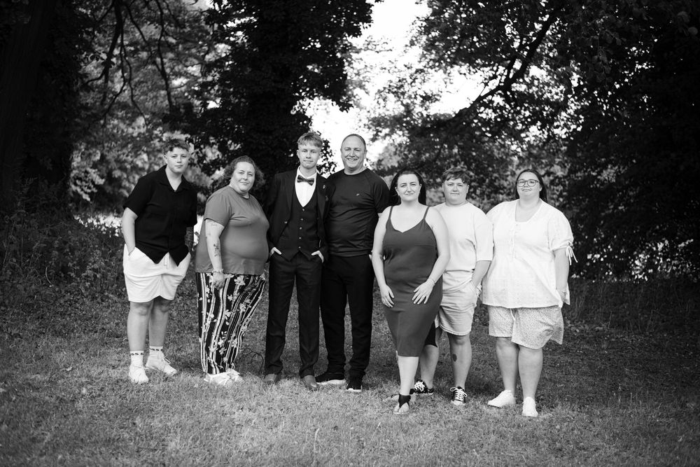 A black and white photo of a group standing together on grass with trees behind them.