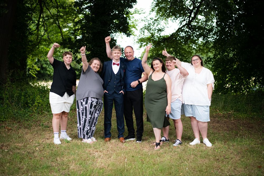 A group of people standing together outdoors on a grassy area with trees in the background.